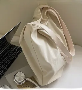 Detail of a cream canvas tote bag styled with a laptop and headphones for a chic work look