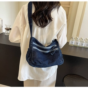 Detail of blue denim crossbody bag with multiple zippers shown in a cafe setting