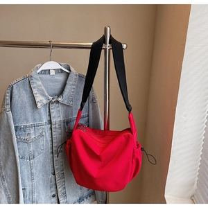 Detail of red nylon crossbody bag with double zippers and black adjustable strap