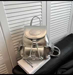 Detail of silver metallic backpack with buckle pockets and high-shine mirror finish texture