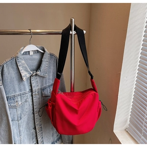 Detail of red nylon crossbody bag with zipper pockets and adjustable wide black strap