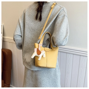 Detail view of yellow bucket bag with horse charm pendant and adjustable strap