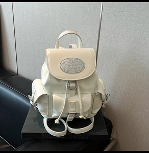 Detailed view of the cream white leather backpack with metal logo and multi-pocket layout