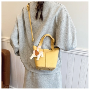 Detail of yellow lychee leather bucket bag with a white horse charm worn by a model