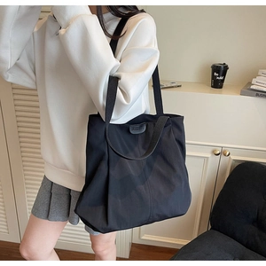 Detail of a large black canvas tote bag with a leather label and casual shoulder strap style