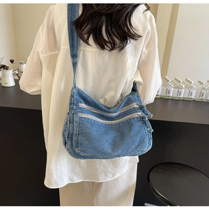 Detail of blue denim tote bag featuring three zipper pockets and washed texture on a model