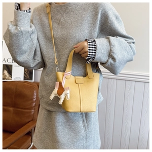 Model showcasing a bright yellow litchi leather bucket bag with a detachable strap