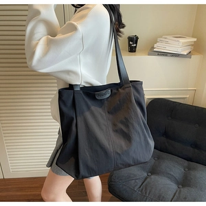 Detail of minimalist black nylon tote bag showing leather JUMAITU label and shoulder strap
