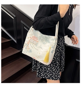 Detailed embroidery of Chinese landscape and yellow tassel on a beige bucket bag