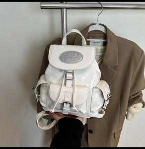 Detail of a white faux leather backpack with silver metal logo and drawstring closure