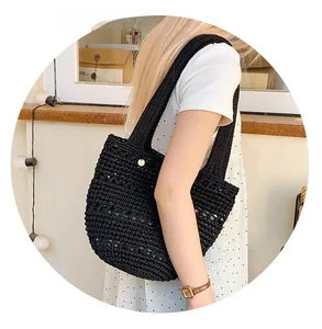 Detail of a black woven half-moon shoulder bag with golden hardware on a female model