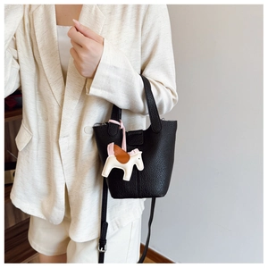 Detail of black pebbled leather bucket bag with a colorful horse charm and shoulder strap