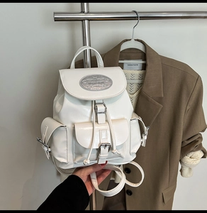 Detail shot of the white glossy PU leather backpack showing silver Moon Shark logo plaque