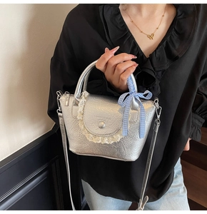 Détail du sac à main argenté métallisé avec bordure en dentelle et nœud à carreaux bleu