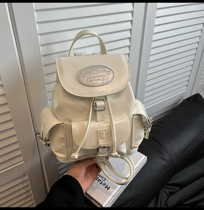 Detail of cream white backpack featuring drawstring closure and silver brand plate