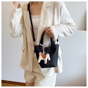 Close-up of black litchi grain leather bucket bag with a colorful horse charm on a model