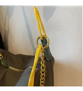 Detail of nylon bag showing golden metal buckle, chain, and yellow woven strap texture