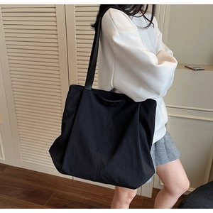 Macro detail of high-capacity black canvas tote bag with wide shoulder strap and leather patch