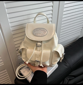 Detail view of cream white mini backpack showing the silver metal logo plaque on the flap