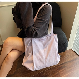 Close-up of lilac canvas tote bag with JUMAITU logo being held by a model in a cozy room