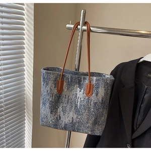 Detailed view of sequined denim tote bag with brown leather handles on a hanger