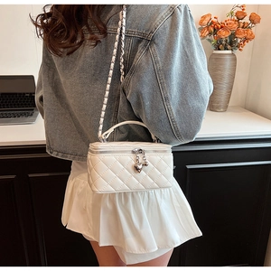 Close-up of quilted white leather crossbody bag with silver chain and heart pendant