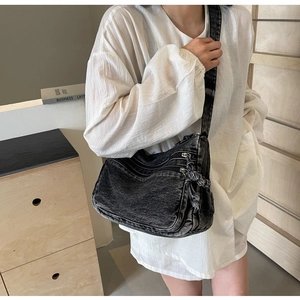 Detail of black denim crossbody bag with fringe trim and multi-zippered pockets