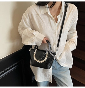 Détail d'un sac à main noir brillant avec bordure en dentelle et nœud à carreaux élégant