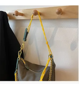 Detail of taupe nylon dumpling bag with yellow rope strap and golden metal chain link