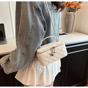 Detail of quilted white crossbody bag with heart charms and metal chain strap on model