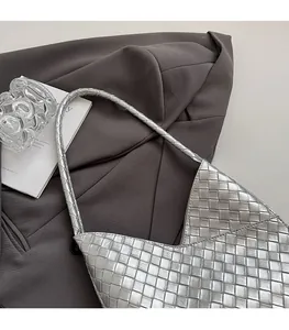 Détail d'un sac à bandoulière tressé argenté avec des lanières cylindriques sur fond gris