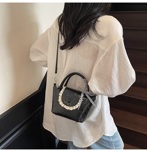 Détail du sac seau en cuir verni noir avec bordure en dentelle et nœud à carreaux