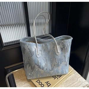 Detail of blue denim tote bag featuring silver sequins and metallic braided handles