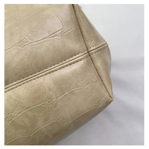 Macro-opname van beige leer met krokodillenreliëf en fijn stiksel op de tote bag