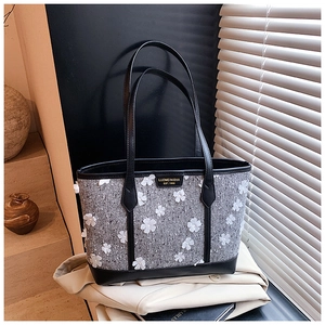 Detail of grey tweed tote bag with 3D white flower appliques and black leather handles