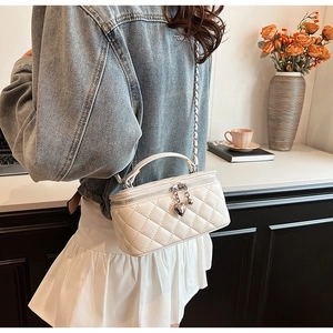 Detail of white quilted crossbody bag with silver heart pendant and metal chain strap