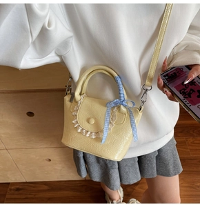 Détail du sac seau en cuir plissé jaune avec bordure en dentelle et nœud en ruban bleu