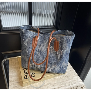 Detail view of denim tote bag featuring silver sequins and brown leather straps on a stone stand