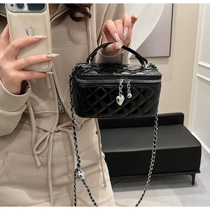 Detail of black quilted leather box bag featuring silver heart charm and chain strap