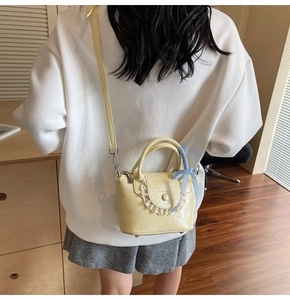 Détail d'un sac bandoulière jaune en cuir ciré avec bordure en dentelle et nœud à carreaux