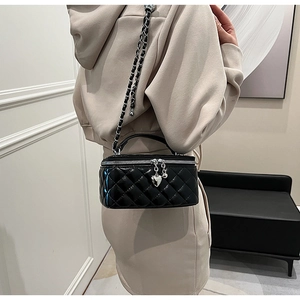 Detail view of a black quilted crossbody bag featuring a chic silver heart charm and chain