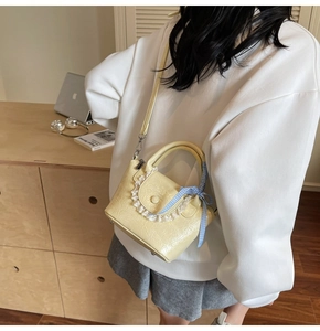 Détail d'un sac seau jaune pâle avec bordure en dentelle et ruban à carreaux bleus