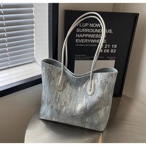 Detail of light blue denim tote bag featuring vertical silver sequins on a metal table