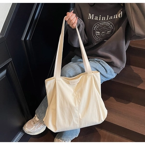 Detail of a large cream canvas tote bag with an embossed leather brand tag on stairs