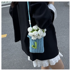 Detail of blue crochet bucket bag with white knit flower, green leaves and bead accents