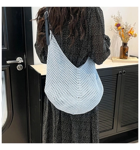 Close-up of light blue crochet knit shoulder bag with hollow mesh design and black strap