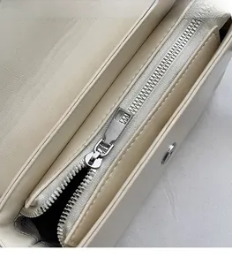 Detail view of the silver metal zipper and smooth litchi grain texture on the beige handbag