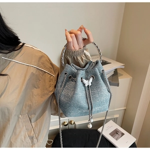 Detail of light blue bucket bag with glitter finish, silver ring handle and pearl butterfly charm
