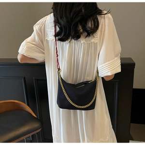 Detail of black nylon hobo bag with gold metal chain and braided shoulder strap shown on model