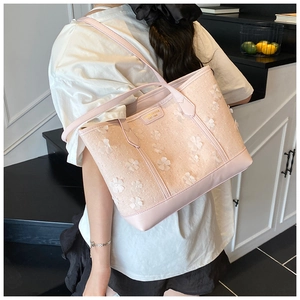 Detailed view of light pink woven tote bag featuring decorative 3D floral appliques and leather straps